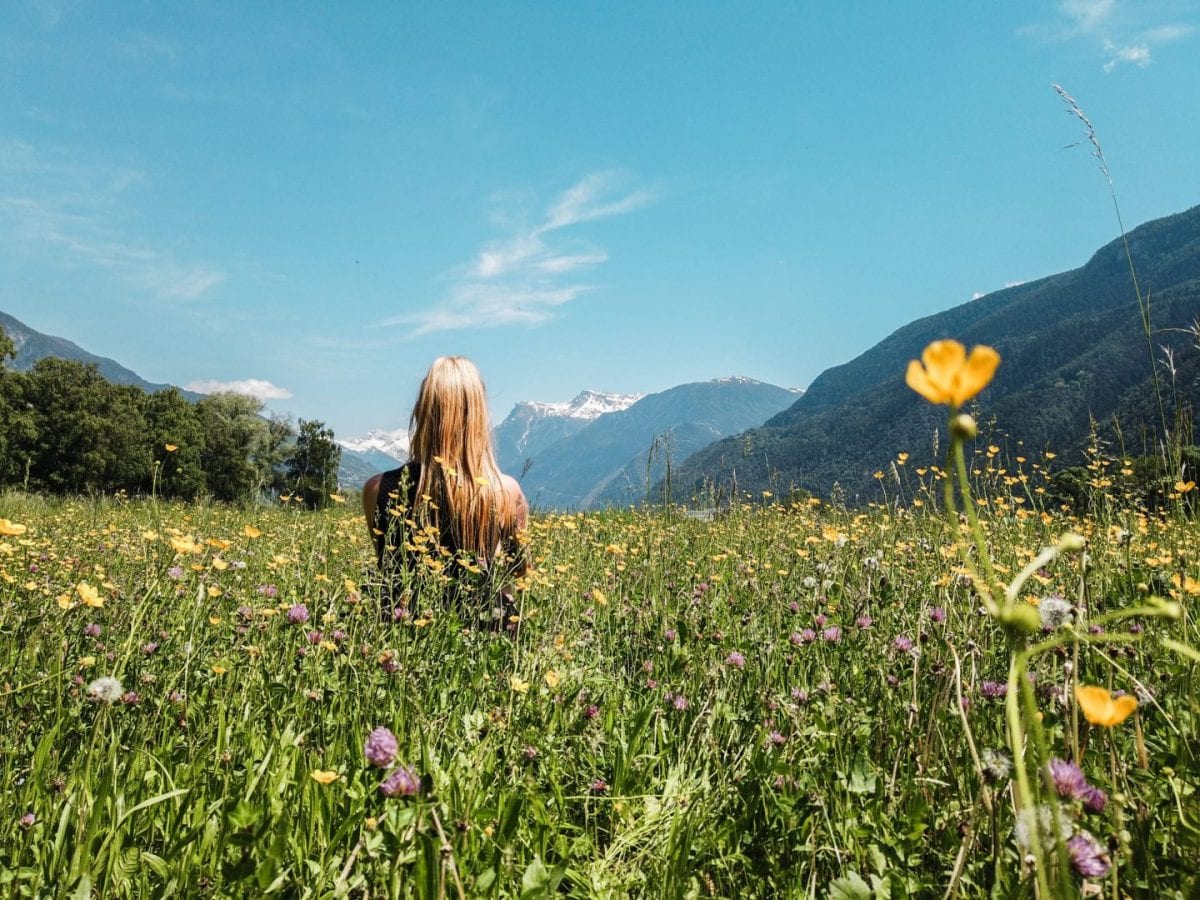 Miriam sitzt auf einer bunten Blumenwiese, im Hintergrund sieht man die schneebedeckten Berge des Wallis, Schweiz.