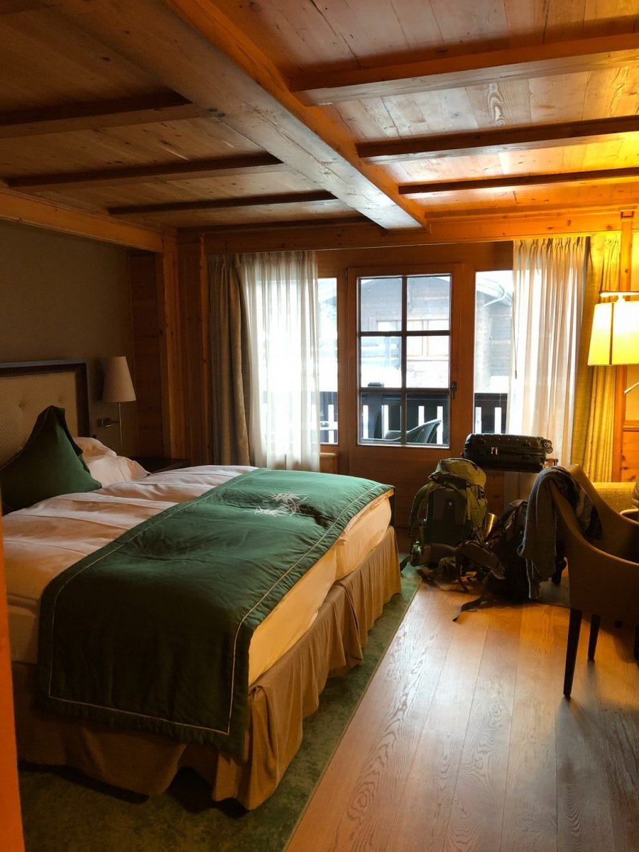 Das Zimmer im Riffelalp Resort. Links ein großes Bett, rechts ein gemütlicher Stuhl. Im Hintergrund der Balkon.