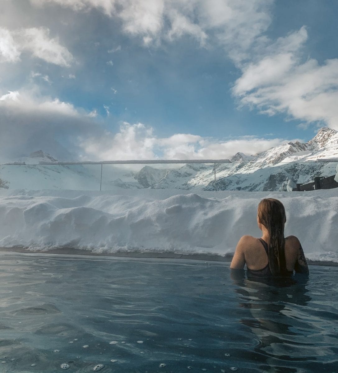 Miriam schwimmt im Outdoor Pool des Riffelalp Resorts mit Blick auf die schneebedeckten Berge