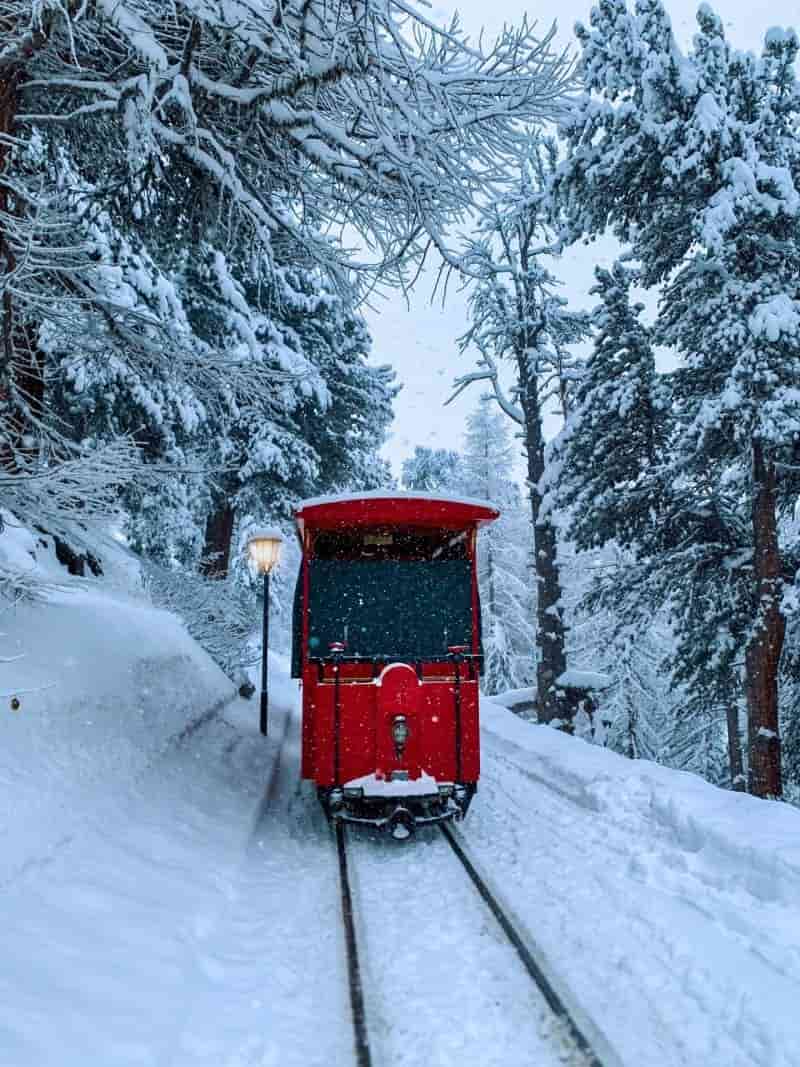 Eine kleine Rote Tram fährt durch einen Winterwald zum Riffelalp Resort
