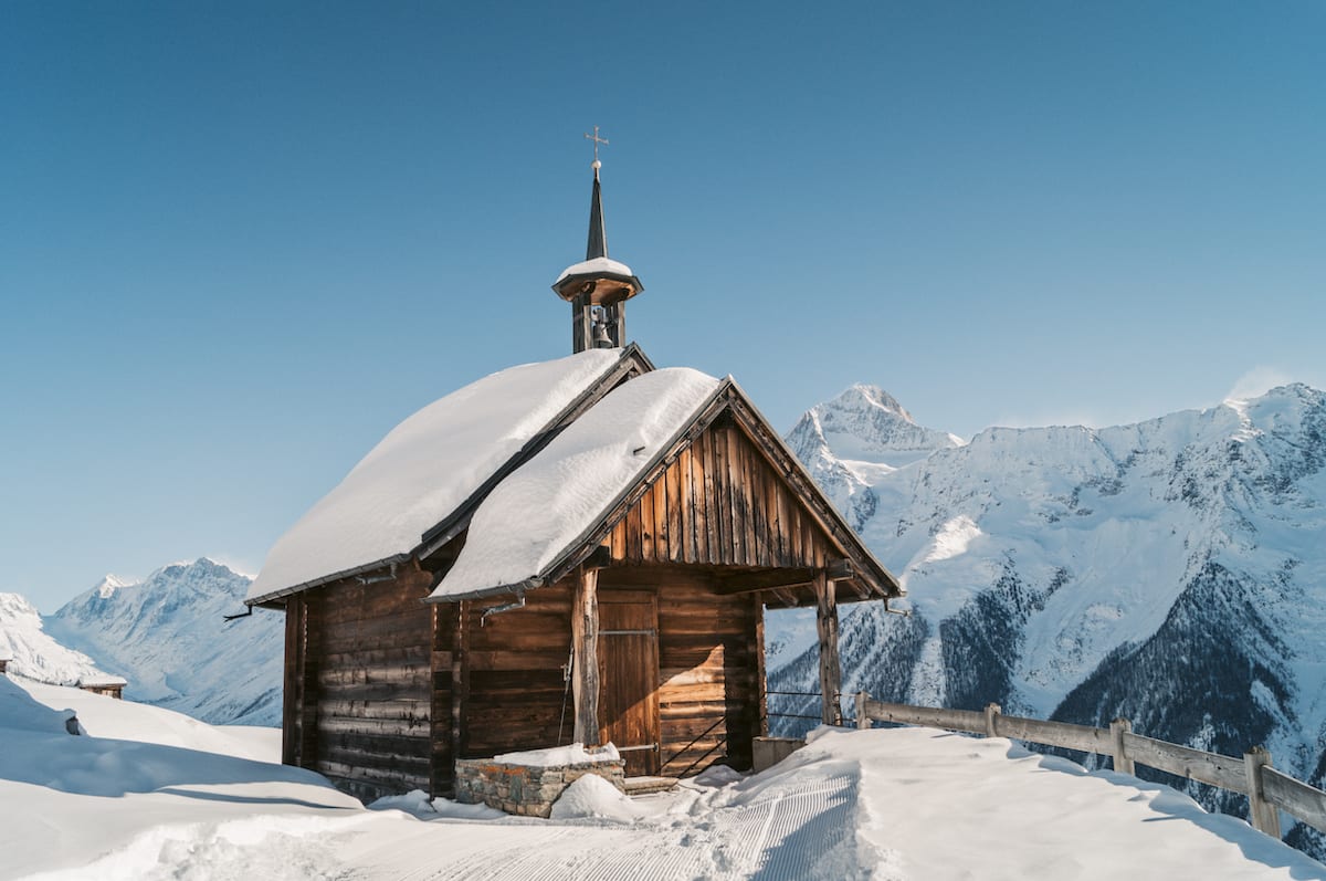 Hölzerne schneebedeckte Kirche vor blauem Himmel und schneebedeckten Bergen
