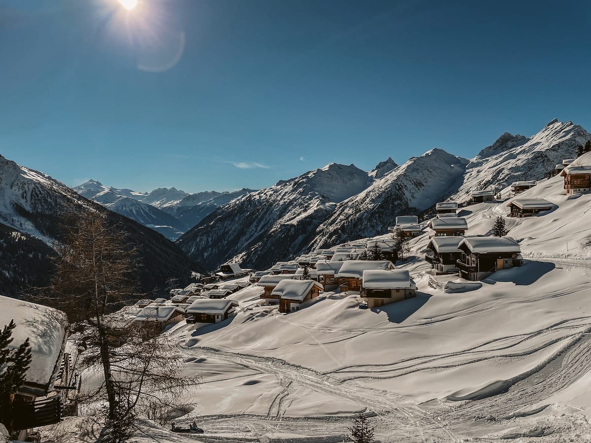 Blick über die Lauchernalp im Lötschental. Viele kleine, schneebedeckte Häuser vor einem weitläufigen Alpenpanorama.
