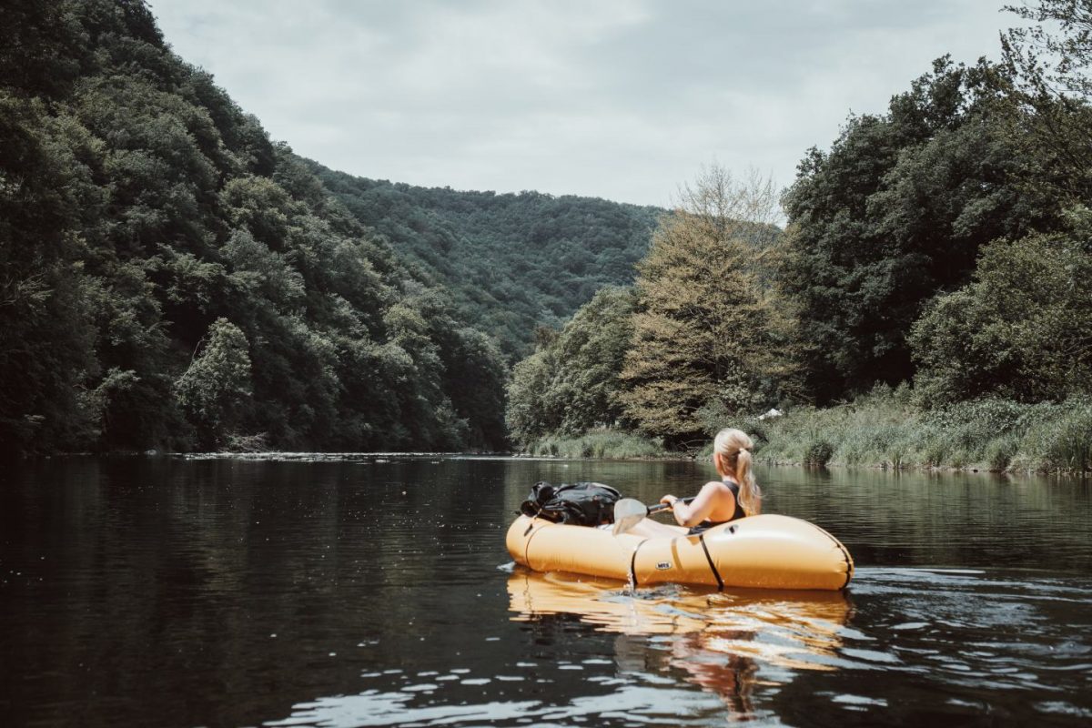 Frau auf Packraft auf dem Wasser umgeben von dichtem Wald in den Ardennen, Frankreich